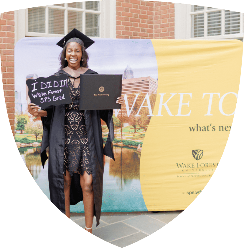 Wake Forest SPS graduate standing in front of WFU signage holding up her degree
